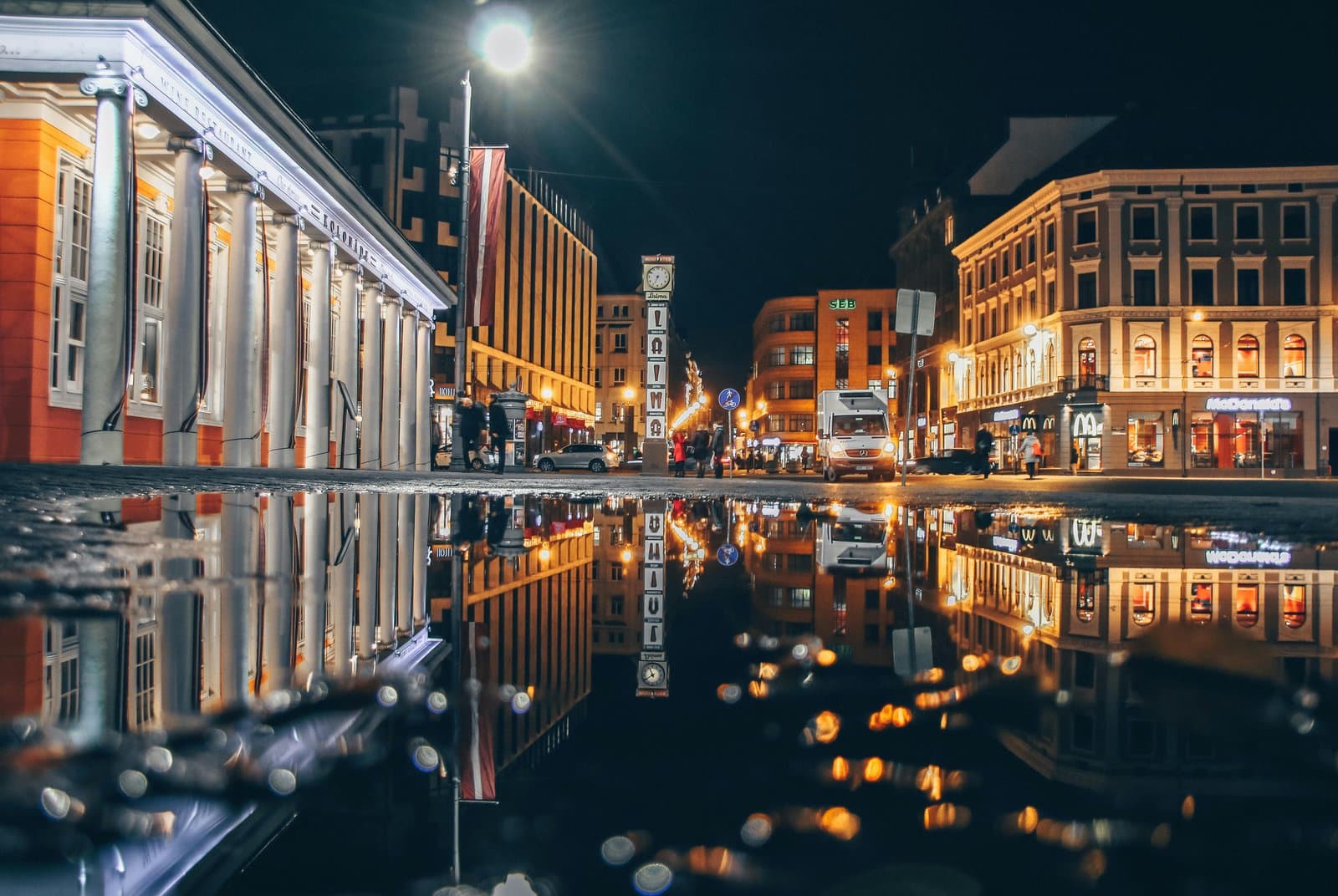 Captivating night view of Riga's city architecture reflected in a puddle, showcasing urban vibrancy.