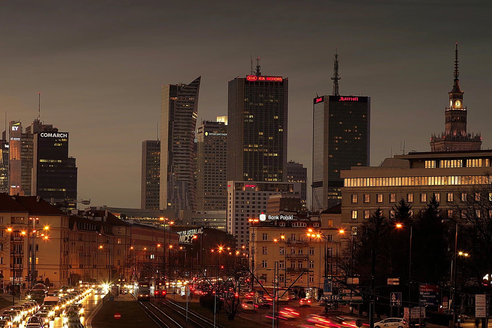 Explore the vibrant night cityscape of Warsaw with illuminated skyscrapers and bustling streets.
