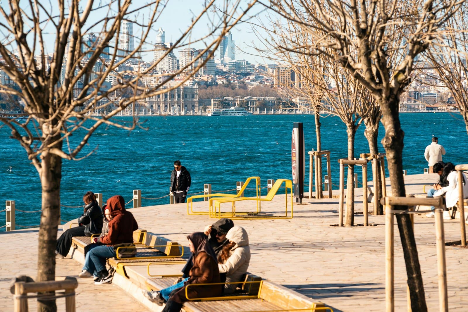 People enjoy a sunny day by the water with a striking view of Istanbul's skyline in the background.
